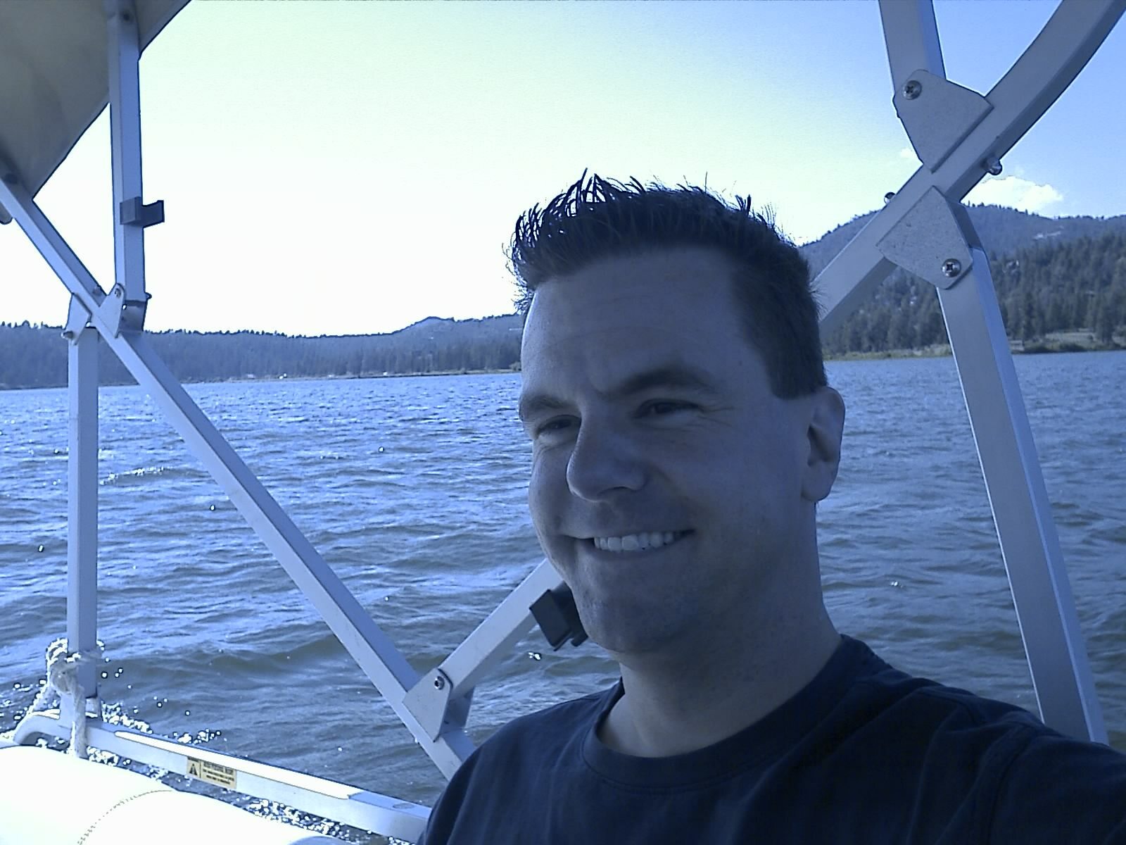 Roger on a boat with lake and mountains behind him at Big Bear
