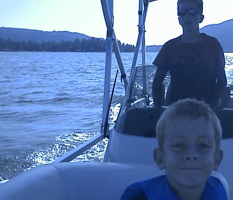 Roger's two sons on a boat with Big Bear Lake and mountains behind them
