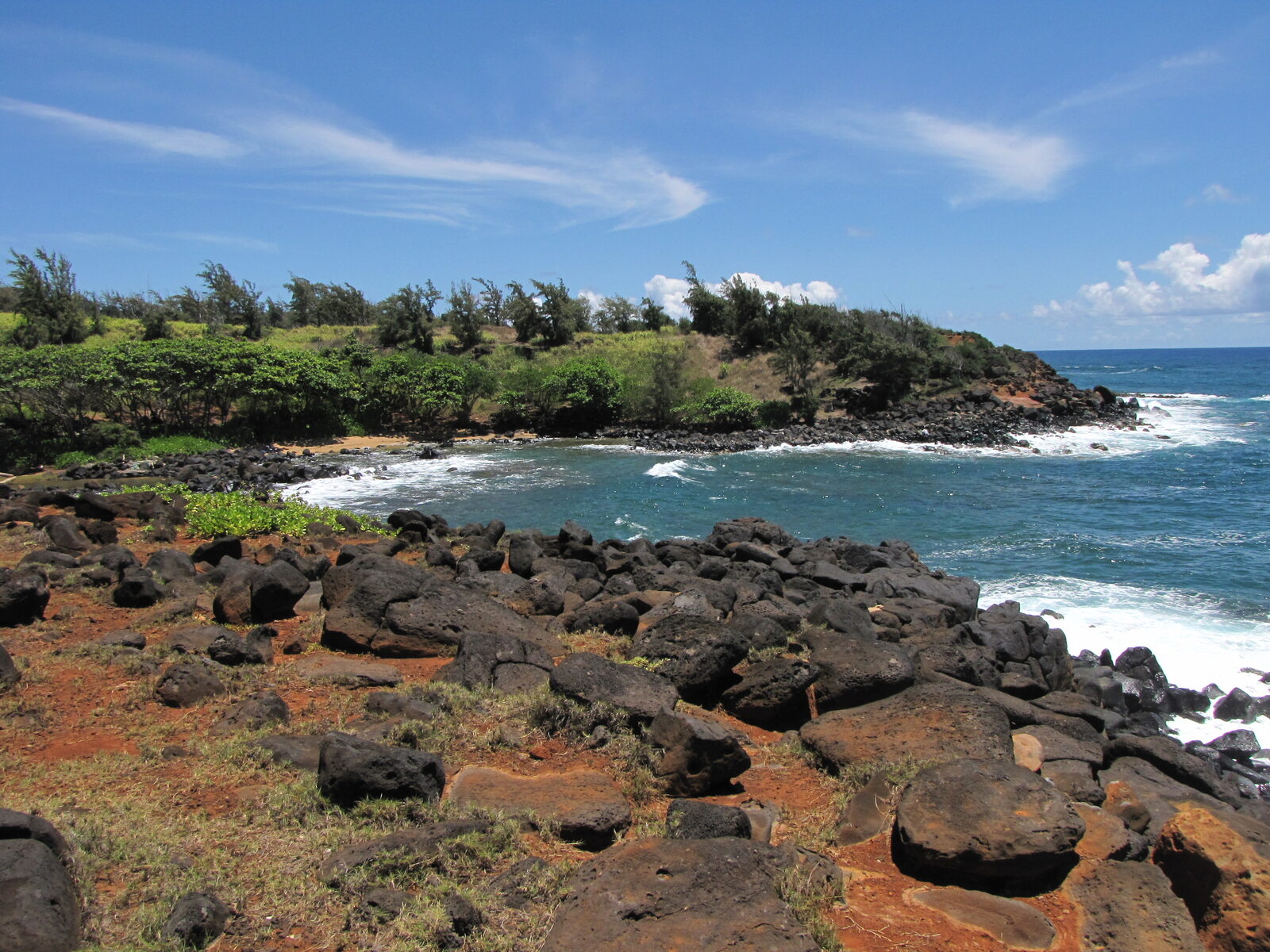 Rocky Kauai coastline with turquoise water and bright clouds