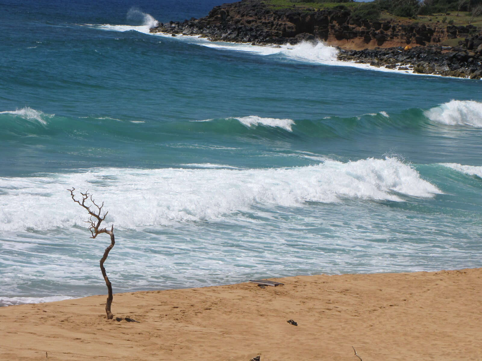 Turquoise surf rolling into a sandy cove on Kauai