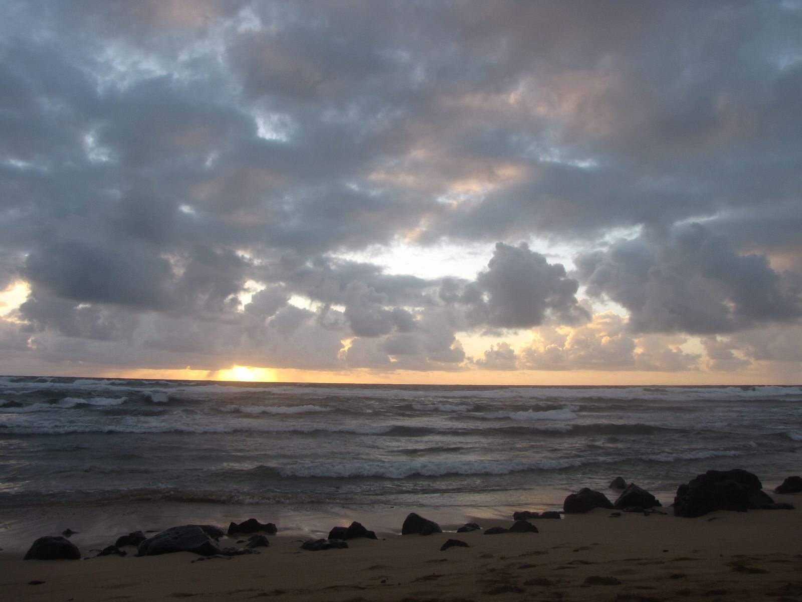 Sun breaking through clouds over a Kauai beach